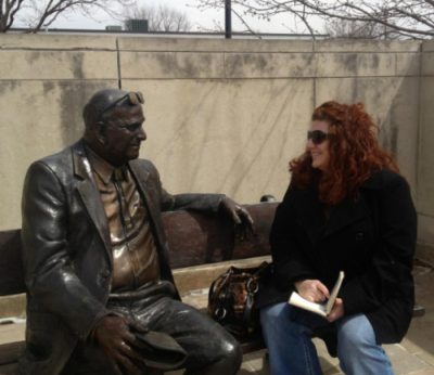 Susan Martens and a sculpture of Cliff Hillegass sitting on a bench